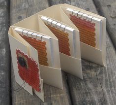 three folded books sitting next to each other on a wooden table with wood planks