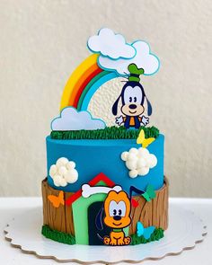 a birthday cake with a cartoon dog on top and rainbow in the sky above it