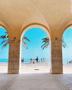 people are walking on the beach under an arch with palm trees in front of them