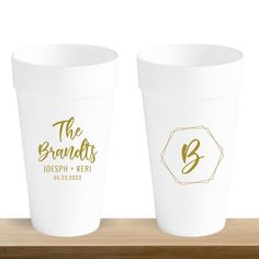 two white plastic cups with gold lettering on the lids and bottom, sitting on a wooden shelf