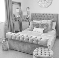 black and white photograph of a bedroom with a bed, mirror, stool and clock