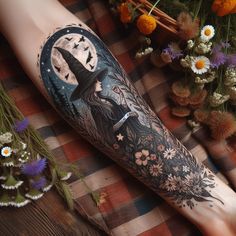 a woman's leg with a tattoo on it that has a witch hat and flowers in the background