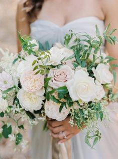 a bride holding a bouquet of white and pink flowers with greenery in her hands