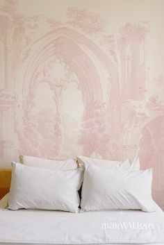 a bed with two pillows on top of it in front of a pink wall mural