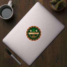 a cup of coffee next to a laptop on a wooden table with an irish themed sticker