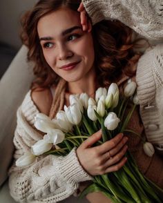 a woman is holding some white flowers in her hands and smiling at the camera while sitting on a couch