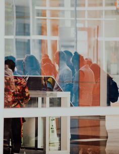 people are standing outside in front of a glass window with the reflection of an orange and blue building