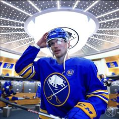 a hockey player wearing a helmet and holding his hand up to his head in front of him