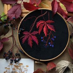 an embroidery project with red leaves and berries on black fabric, surrounded by autumn foliage