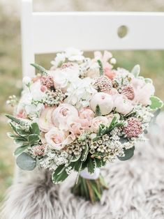 a bridal bouquet sitting on top of a white chair in front of a furry rug