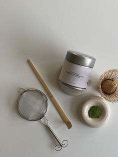 a jar of green tea next to a metal strainer and wooden spoon on a white surface