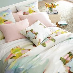 a bed with colorful sheets and pillows in a room next to a vase filled with flowers