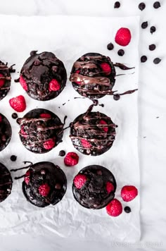 chocolate cupcakes with raspberries and chocolate frosting on white parchment paper