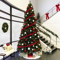 a decorated christmas tree sitting in the middle of a room next to a stair case