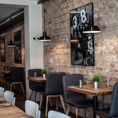 an empty restaurant with wooden tables and black chairs, brick walls and artwork on the wall