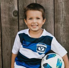 a young boy holding a soccer ball in front of a wooden wall with planks