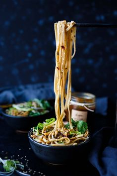 noodles being lifted with chopsticks from a black bowl on a dark tablecloth