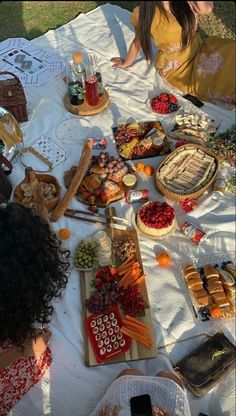 two women sitting at a picnic table with food on it and drinks in front of them