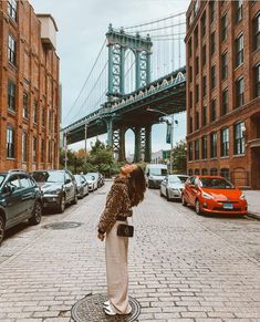 a woman is standing on the sidewalk in front of some cars and a large bridge