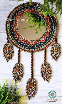 a mirror hanging on the side of a wall with feathers and leaves attached to it