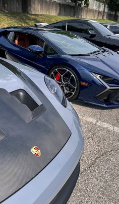 two blue sports cars parked next to each other in a parking lot with grass behind them