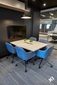 a table with blue chairs in front of a flat screen tv on a wall behind it