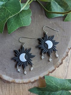 two sun and moon earrings sitting on top of a piece of wood next to leaves