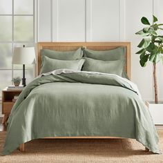 a bed with green sheets and pillows in a room next to a potted plant