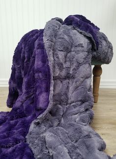 a purple and grey blanket sitting on top of a wooden floor next to a chair