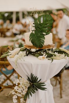 a table topped with a white cake covered in greenery