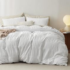 a bed with white comforter and pillows in a small room next to a night stand