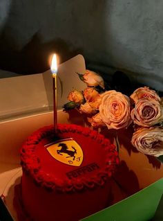 there is a red cake with a ferrari emblem on it and roses in the box