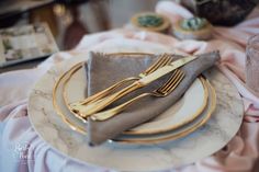 the table is set with silver and gold plates, napkins, and utensils