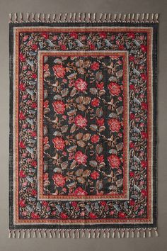 a black and red rug with fringes on the bottom, in front of a gray wall