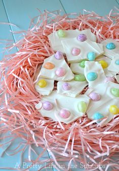 an easter egg bark with white chocolate and colorful candies on it in a pink nest