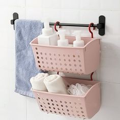 two pink baskets are hanging on the wall next to towels and soaps in front of a towel rack