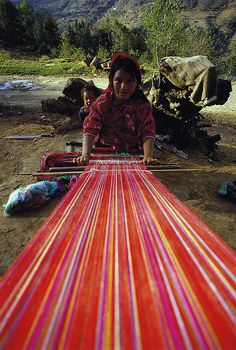 a woman sitting on the ground next to a red and yellow striped blanket with mountains in the background