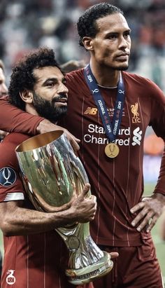 two soccer players are hugging each other with the trophy in their hands and one has his arm around the other's neck