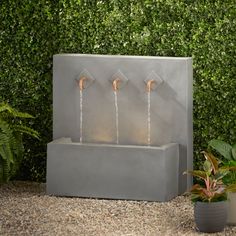 an outdoor fountain with three faucets in the center and two plants behind it