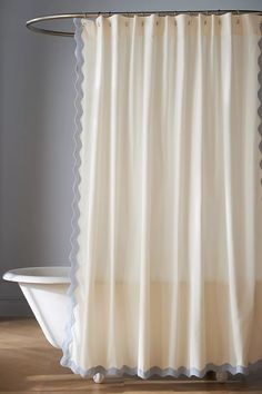 a white shower curtain with scalloped edges in front of a bathtub and wooden floor