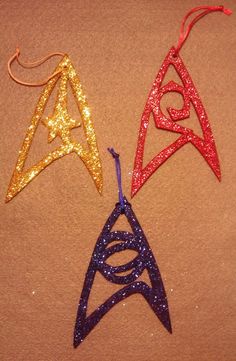 three star trek inspired ornaments are shown on a brown surface with gold and red glitter