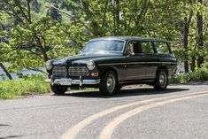 an old black car is parked on the side of the road in front of some trees