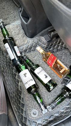 four bottles of alcohol sit in the back seat of a car, next to an empty bottle