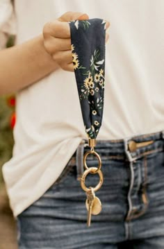 a woman holding onto a black and white flowered pocket scarf with gold keychain