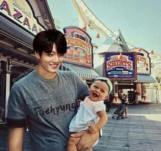 a man holding a baby in front of a carnival