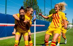 three female soccer players in yellow and red uniforms are celebrating on the field with their arms around each other