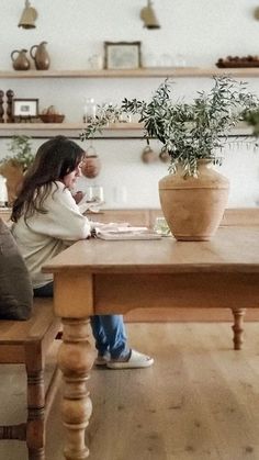 a woman sitting at a wooden table with a potted plant on top of it