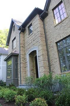 a large brick house with lots of windows and bushes in the front yard, next to it