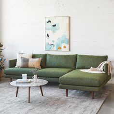 a living room with a green couch and coffee table in front of a white brick wall