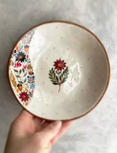 a hand holding a bowl with flowers painted on it